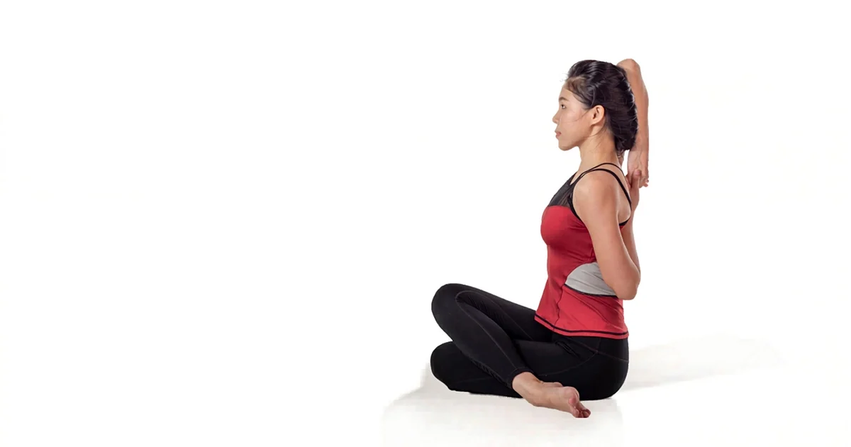 A yoga practitioner demonstrates proper spine elongation and stacked knee alignment in Gomukhasana.