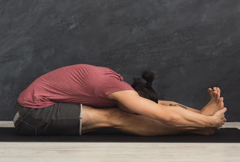 A yoga practitioner demonstrates proper pelvic tilting and safe spinal lengthening while holding Paschimottanasana.