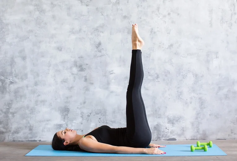 A yoga practitioner demonstrates a flat lower back and legs extended vertically at a ninety degree angle in Ardha Halasana.