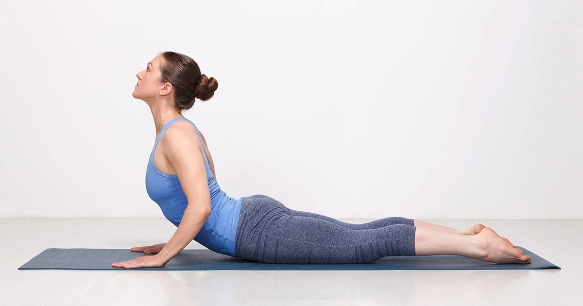 A yoga practitioner keeping her shoulders drawn back away from her ears while showing correct alignment in Bhujangasana.