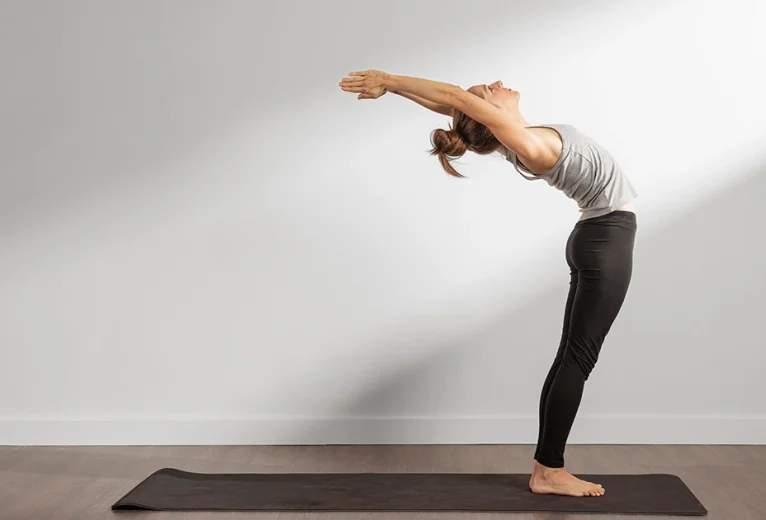 A practitioner demonstrates Ardha Chakrasana by supporting the lower back with both hands while gently arching the upper spine backward.