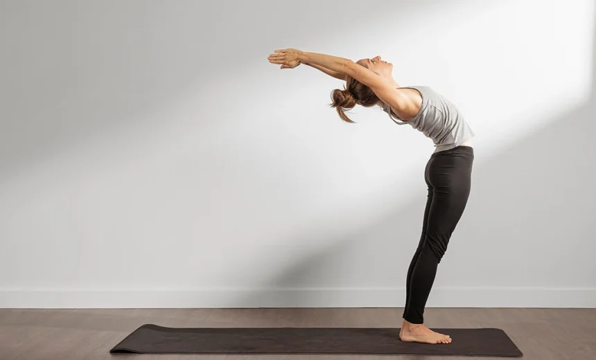 A practitioner demonstrates Ardha Chakrasana by supporting the lower back with both hands while gently arching the upper spine backward.