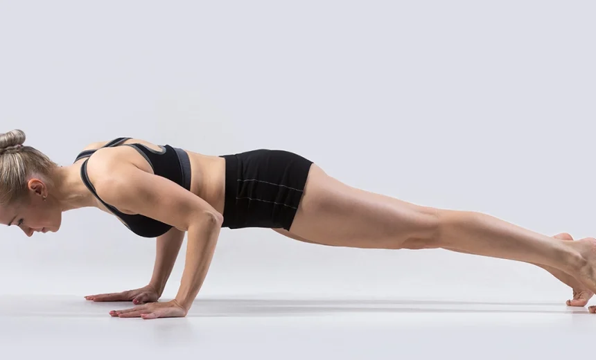A practitioner demonstrates the correct hover alignment of Chaturanga Dandasana on a blue mat, maintaining the shoulders at elbow height.
